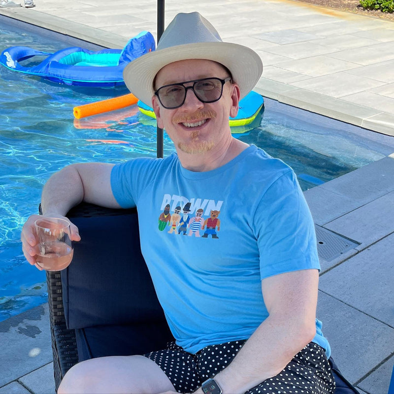 A man in a sun hat by the pool in the light blue Provincetown Mates tee