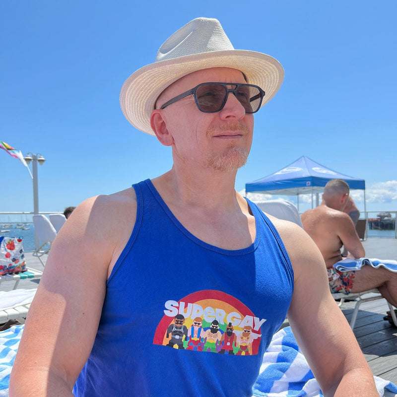 A man in a straw hat at the beach in the blue Super Gay Mates tank
