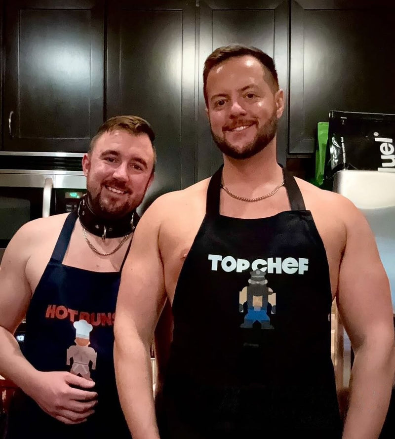 Two men in a kitchen wearing the Top Chef and Hot Buns aprons